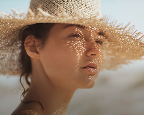 Närbild av kvinnas ansikte i starkt solljus, skyddad av en solhatt