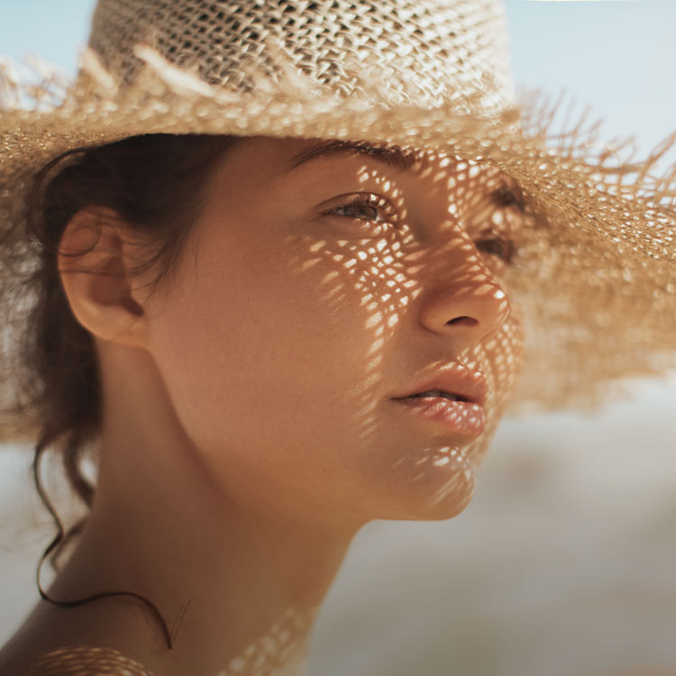 Närbild av kvinnas ansikte i starkt solljus, skyddad av en solhatt