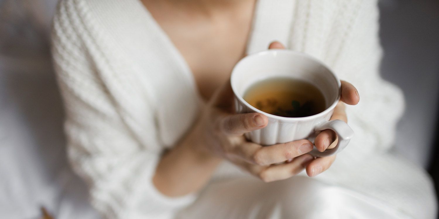 Kvinna i lugn hemmiljö som håller en kopp varmt te i båda händerna.