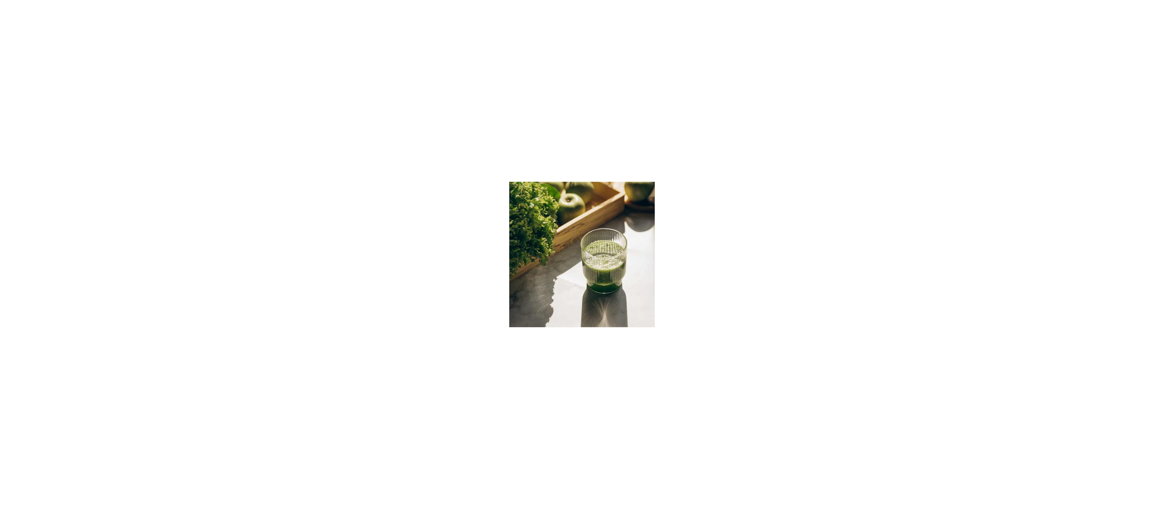 A glass of green smoothie lit by sunlight, next to kale and apples