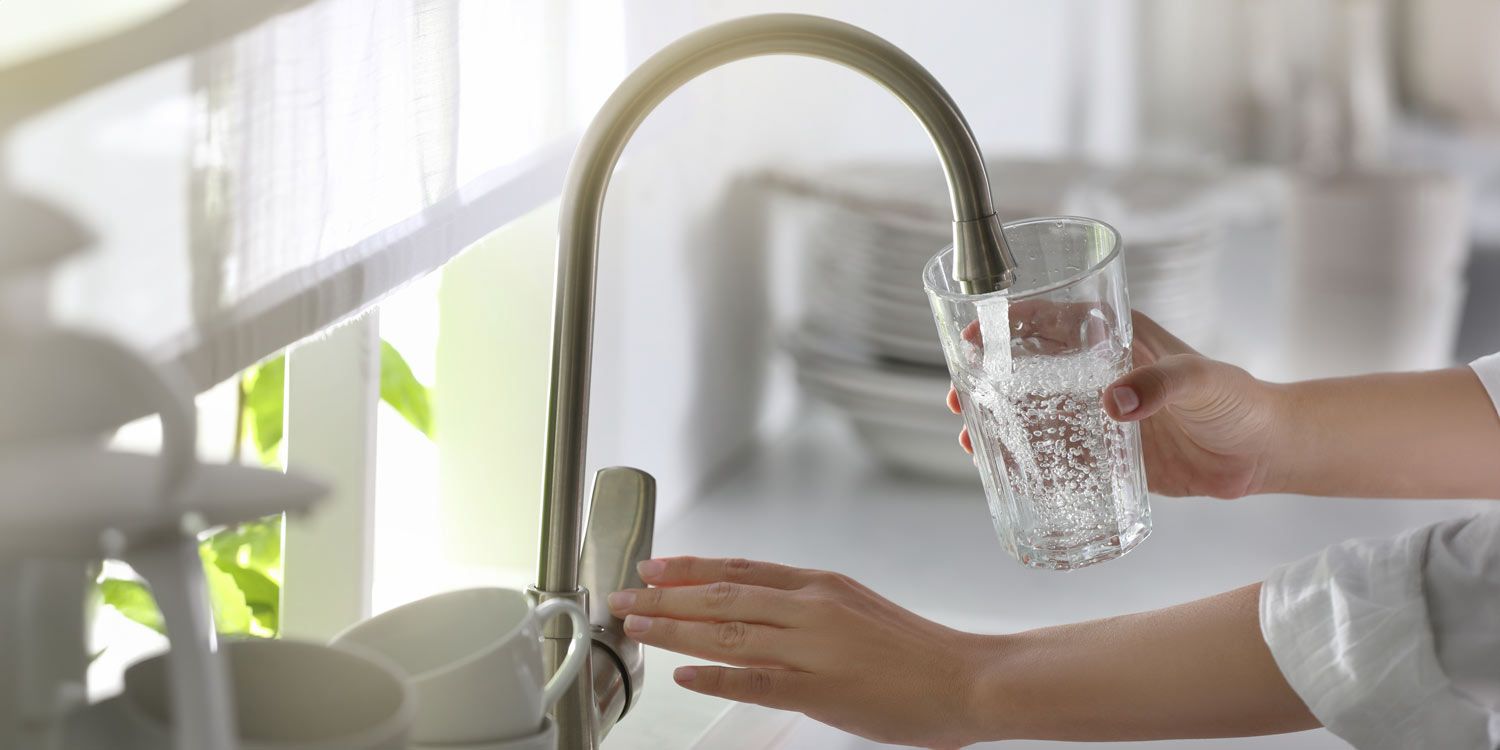 A glass of water is filled with tap water in a bright kitchen environment