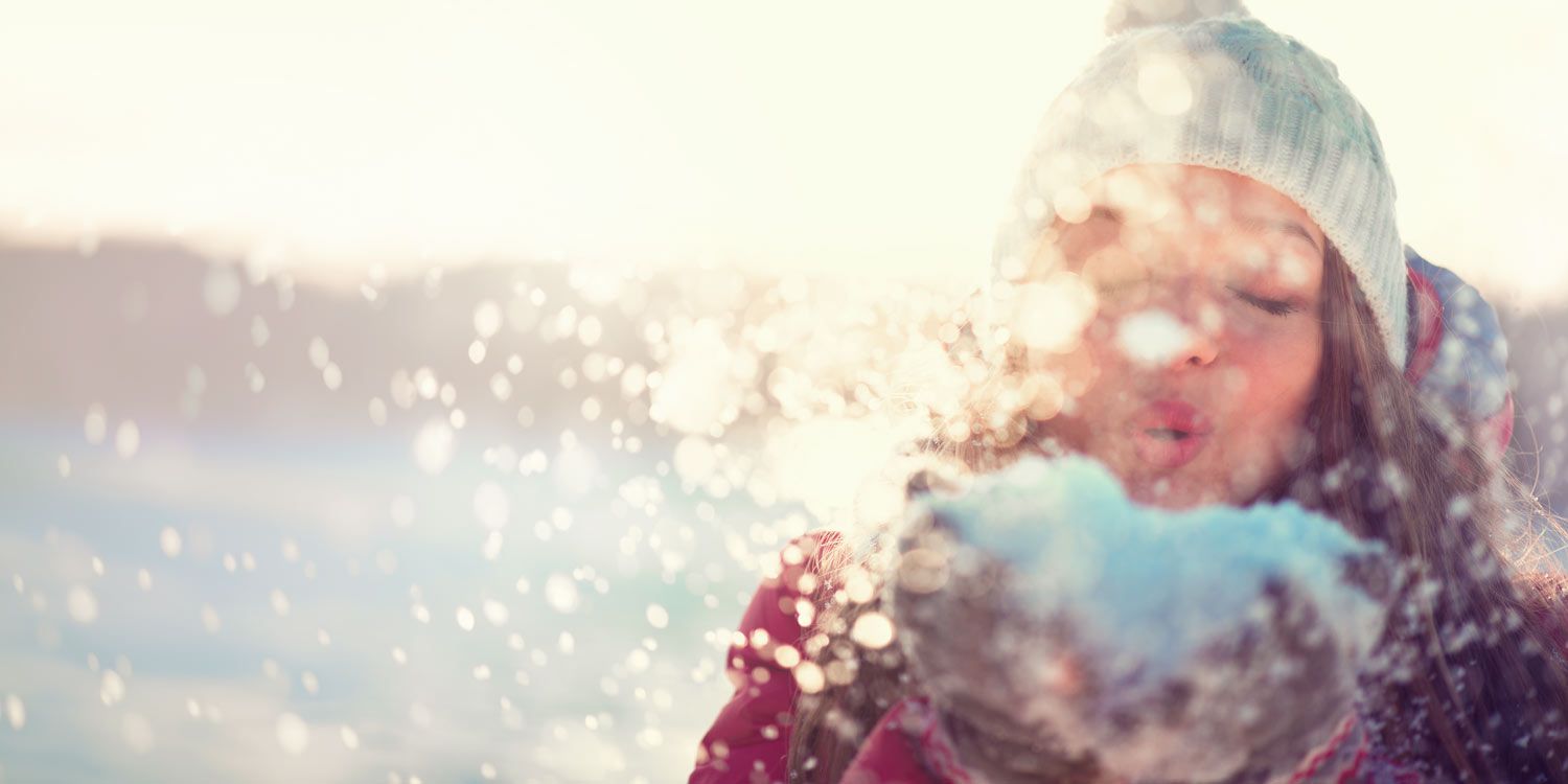 Kvinna blåser en hög med snö i ett soligt vinterlandskap