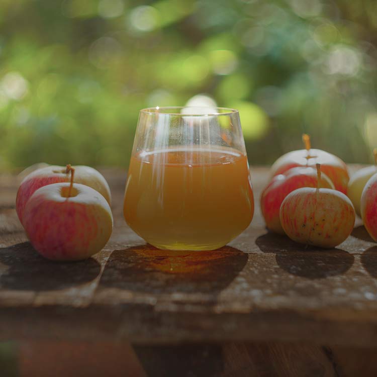 Glas med äppelcidervinäger bredvid färska äpplen.