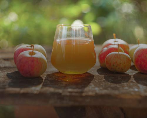 Glas med äppelcidervinäger bredvid färska äpplen.