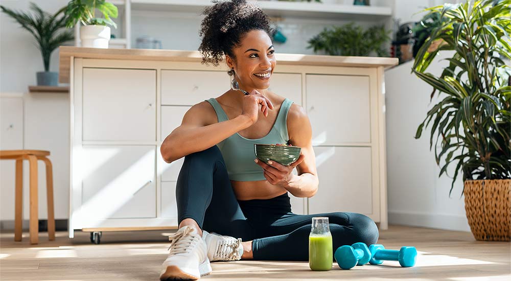 Woman with active wear on is eating a bowl and looks healthy 