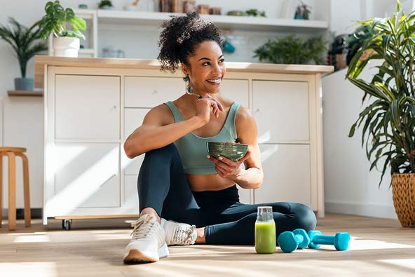 Woman with active wear on is eating a bowl and looks healthy 