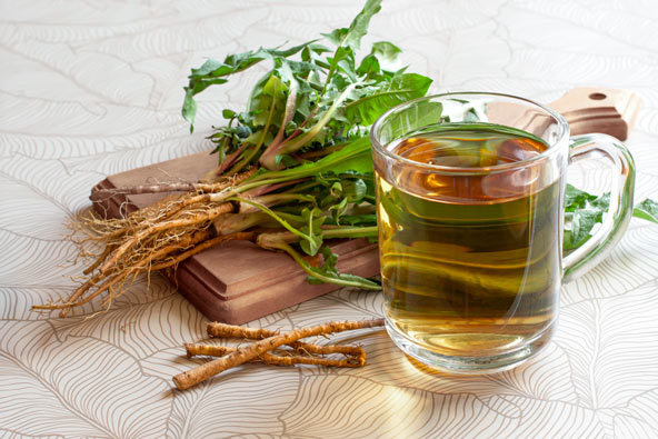 Dandelion roots on a cutting board next to a cup of dandelion tea