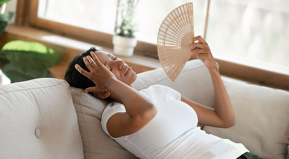 Tired and hot woman sits on a sofa and fans herself with a fan