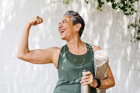 Happy woman wearing workout clothes holding up her arm to show her muscles