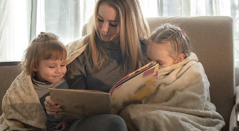 Mamma läser en barnbok för sina två små barn som är inlindade i mysiga filtar