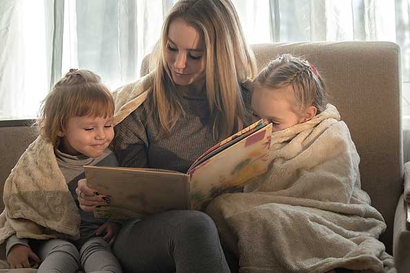 Mother reads a children's book to her two small children who are wrapped in cozy blankets