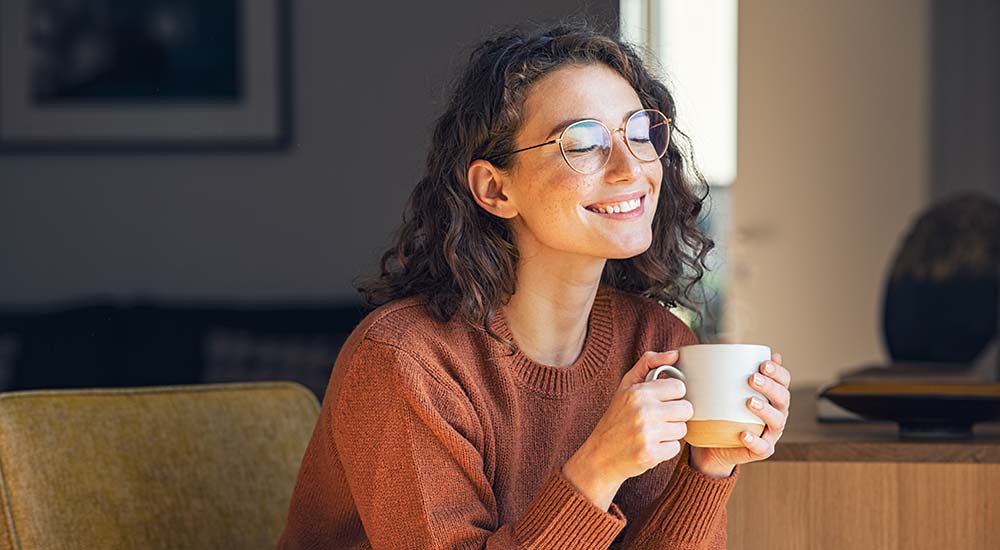 Glad kvinna njuter av en varm kopp te i sitt hem