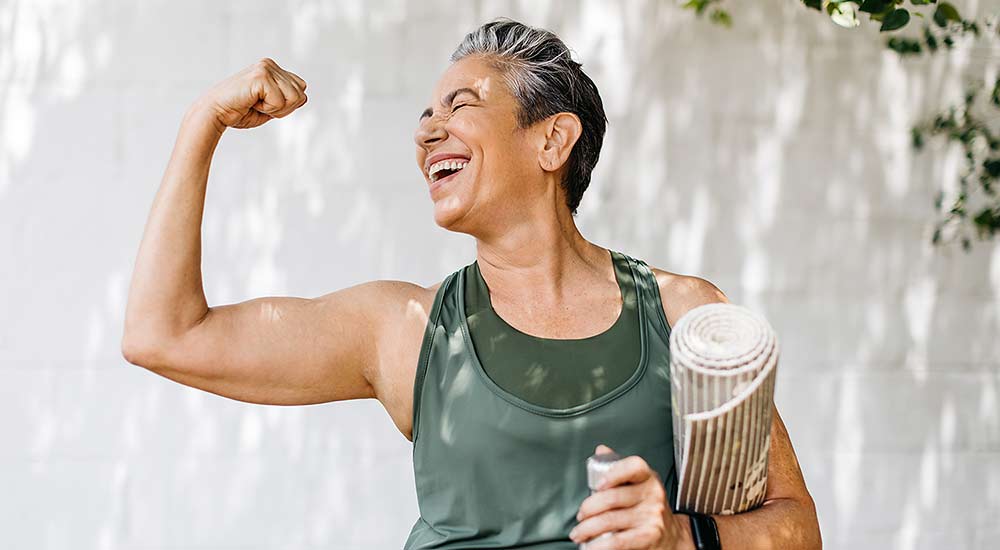 Happy woman wearing workout clothes holding up her arm to show her muscles