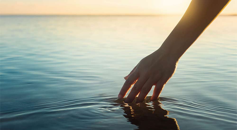 En hand som rör vid vattenytan i en sjö vid solnedgång