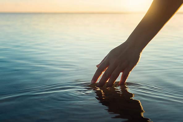 En hand som rör vid vattenytan i en sjö vid solnedgång