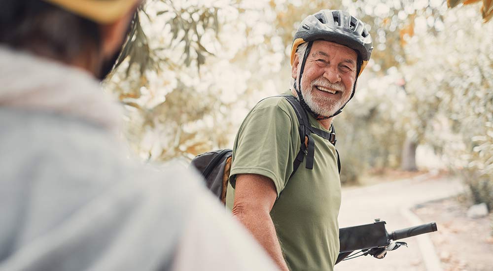 Happy man in his sixties standing outside in nature by his bicycle and smiling at a friend