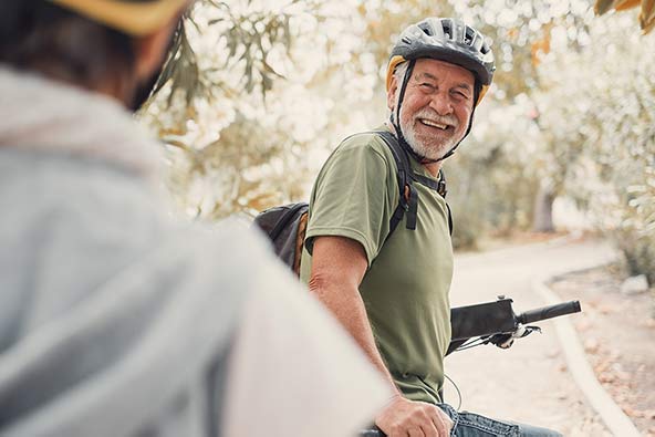 Happy man in his sixties standing outside in nature by his bicycle and smiling at a friend