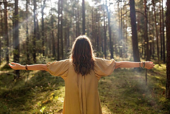 Kvinna som står i skogen och njuter av solen