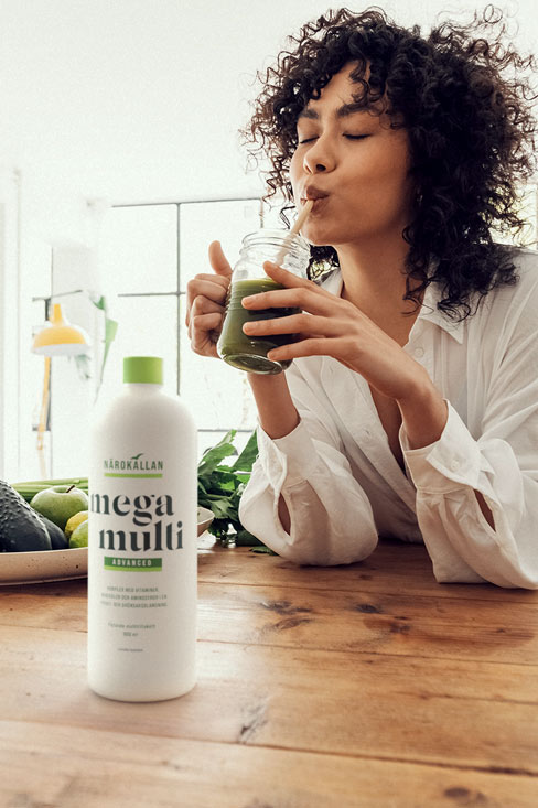 Woman sipping a green smoothie next to a bottle of Närokällan Mega Multi liquid multi vitamin