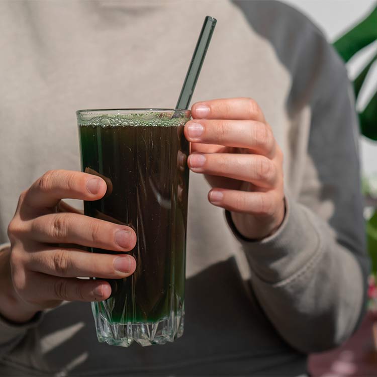 Kvinna håller i ett glas med mörkgrön dryck