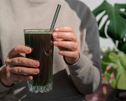 Kvinna håller i ett glas med mörkgrön dryck