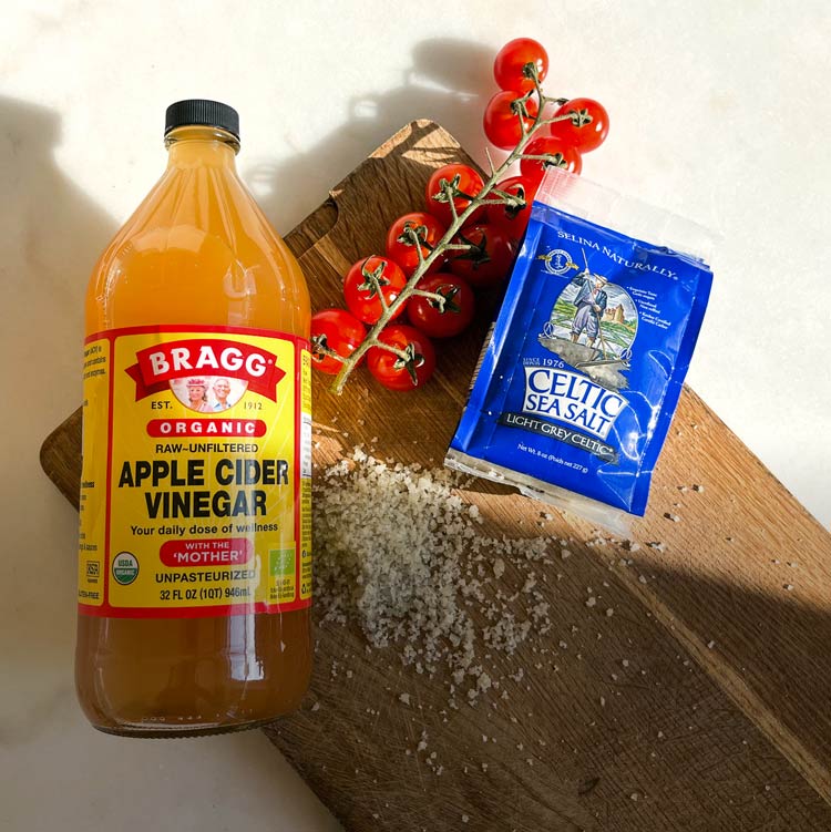 Äppelcidervinäger från Bragg, havssalt från Celtic Sea Salt och kvisttomater på en skärbräda med ljus bakgrund.