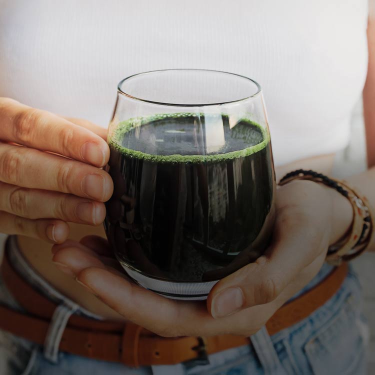 Glas med mörkgrön chlorelladryck i handen