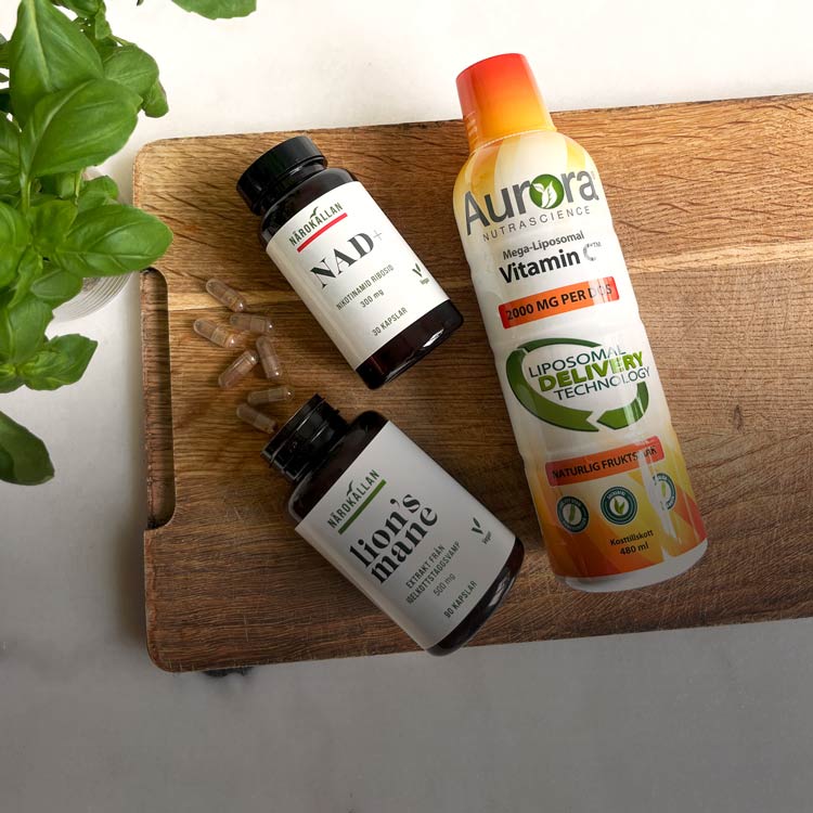 Kosttillskott från Närokällan på en skärbräda: NAD+, Lion’s Mane och liposomal C-vitamin från Aurora. Basilikablad i vänsterkanten.