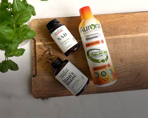 Kosttillskott från Närokällan på en skärbräda: NAD+, Lion’s Mane och liposomal C-vitamin från Aurora. Basilikablad i vänsterkanten.