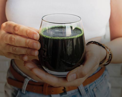 Glas med mörkgrön chlorelladryck i handen